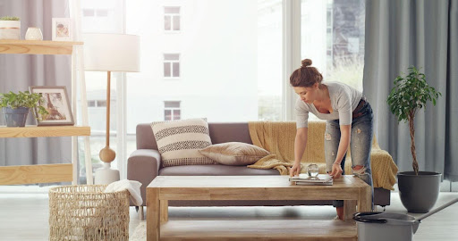Decluttering Indian Homes: Tips for a Calm & Organized Space 3 Woman tidying up a modern, minimalist living room with natural light.